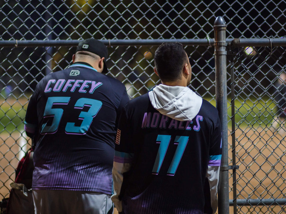 Two players at the dugout fence in custom sublimated baseball jerseys with names and numbers