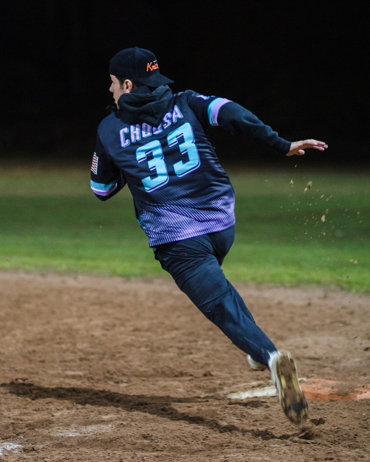 Player rounding a base at night in a custom sublimated 7Bros jersey with name and number